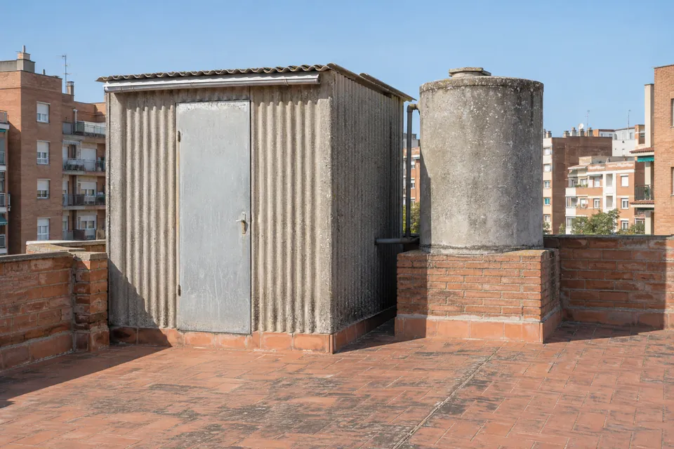 Coberta ondulada i dipòsit d'aigua de fibrociment antics al terrat d'un bloc de pisos