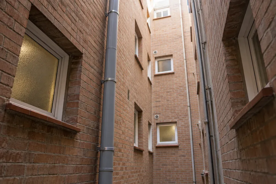 Baixant nou de PVC gris al pati de llums d'un bloc de pisos de maó