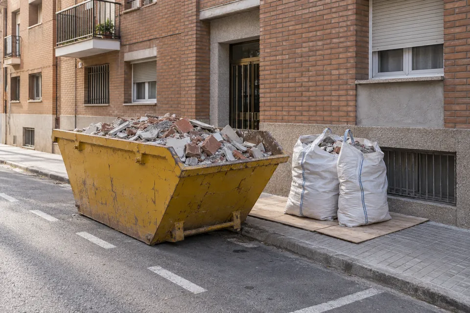 Contenidor de runa i sacs d'obra al costat d'un bloc de pisos