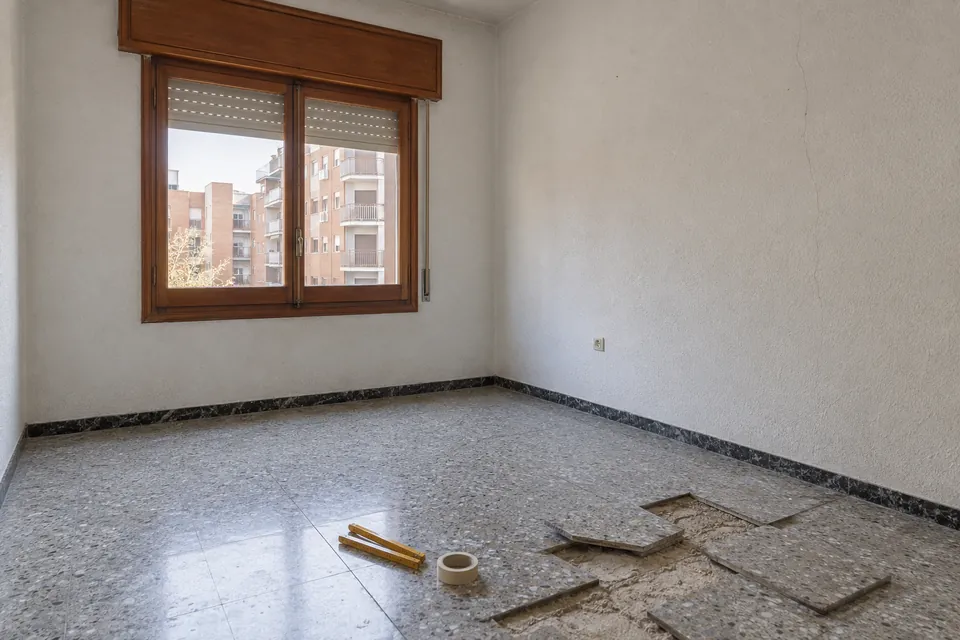 Habitació d'un pis antic abans de la reforma, amb el terratzo aixecat i parets de gotelé