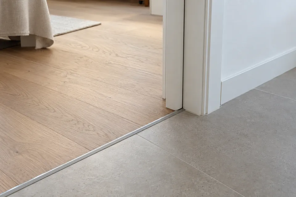 Trobada entre parquet de roure i porcellànic gris al pas d'una porta